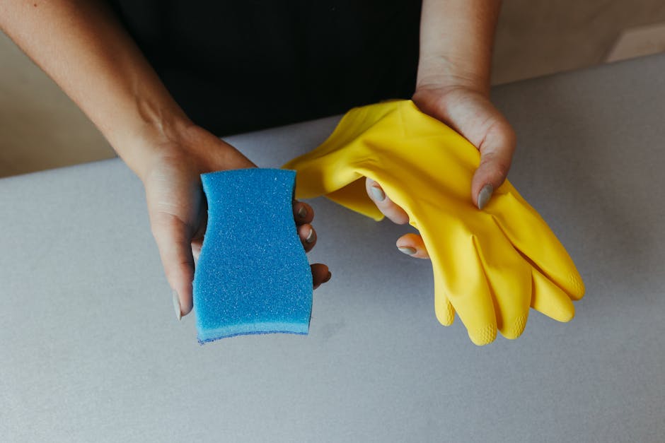 Close-up of hands holding a blue sponge and yellow rubber gloves on a table.