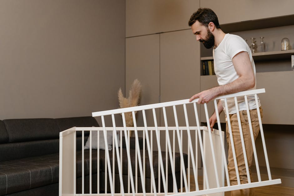 A bearded man assembles a crib in a stylish living room setting.