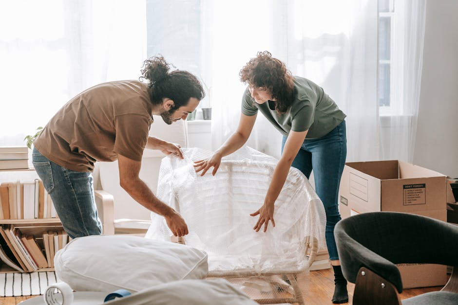 A couple packing furniture with bubble wrap, preparing for relocation in a cozy apartment.